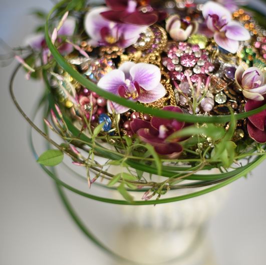 A nosegay of vintage brooches form a cap on this classic garden urn that is veiled with an overlay of Phalaenopsis, Jasminum polyanthum, and Liriope. Photo: Jason Edwards