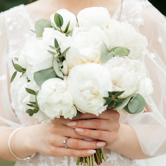 Bridal bouquet featuring white peonies and mixed greenery.
