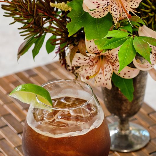 A zippy cocktail paired alongside an arrangement featuring lilies and decorative foliage.