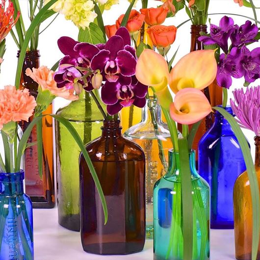 A collection of antique bottles with callas, orchids, carnations, Alstroemerias, and Chrysanthemums. 