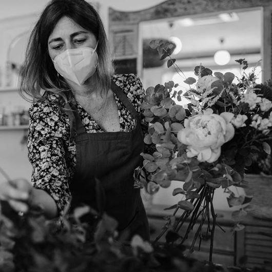 Floral designer with face mask arranging cut flowers during COVID-19 pandemic.